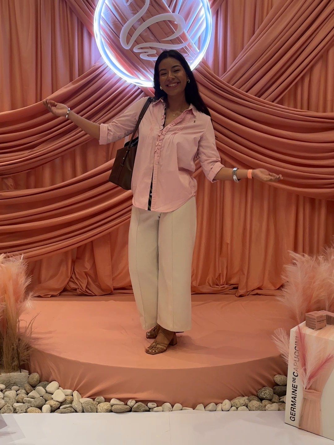 Ambar, sonriente, con blusa rosada en un escenario de cortinas rosadas de un evento de belleza